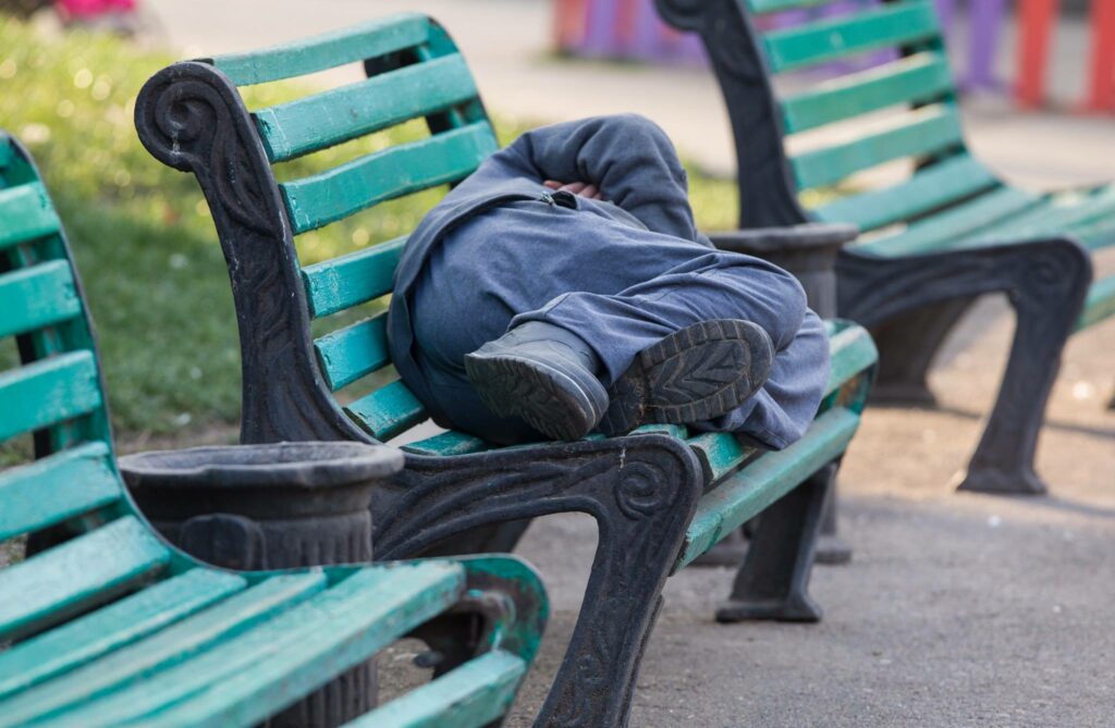 Man sleeping rough outside on a bench in hot weather